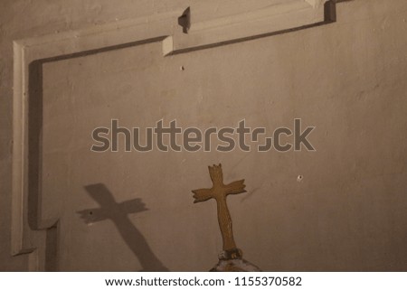 Close up indoor view of a golden wooden station of the cross and its shadow reflected on a white stone wall. Antique object located in a french church. Abstract image, symbol of spirituality and faith