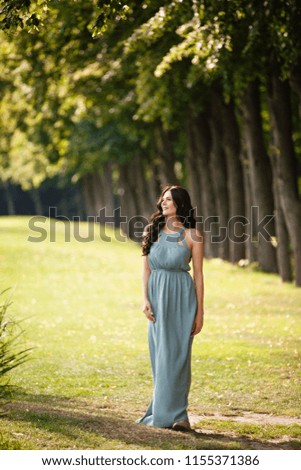 Summer mood. Romantic woman weared in long dress walk in a park on background of line of beautifull trees. Backlight. Spring or summer coming. Spring story. Brown-haired girl with long hairs.