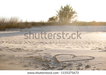 romantic heart drawn in the sand of a beach shone by beautiful evenint sunlight