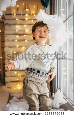 Cute little boy on Cristmas lights background playing with fake snow
