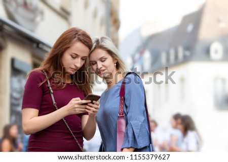 Two attractive young women taking a conversation outside and looking their smartphone 