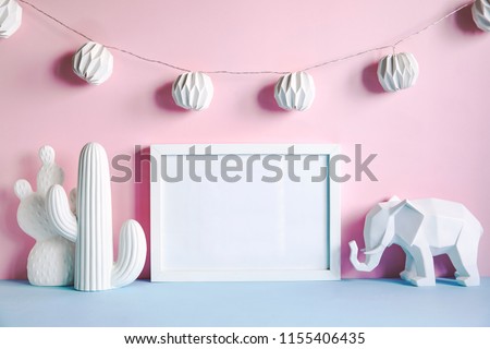 Modern minimalistic desk with mock up photo frame, cacti and elephant figures and hanging cotton lamps. Pink backgrounds wall. Lovely childroom.
