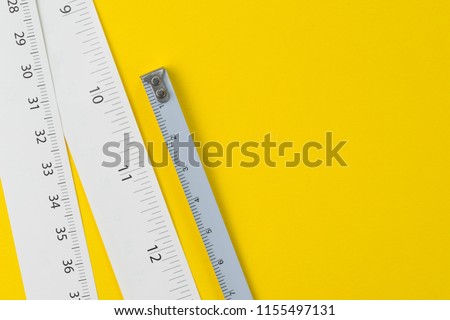 White measuring tapes with centimetre and inches on vivid yellow background with copy space, length, long or maker concept.