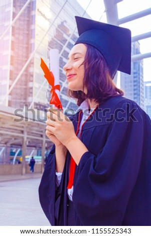 She is  Graduate and wearing  graduate's dress.She standing and show degree certificate.She is celebration education graduation.She is happy in good time.Photo concept  Education and success.
