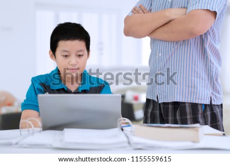 Picture of preteen boy being supervised by her father while studying with a laptop in the living room