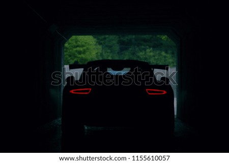Silhouette of supercar in tunnel with stop lights. Rear view of supercar Royalty-Free Stock Photo #1155610057