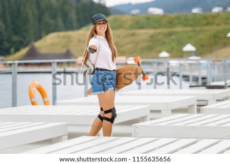Young beautiful girl standing with longboard near the mountain lake beach