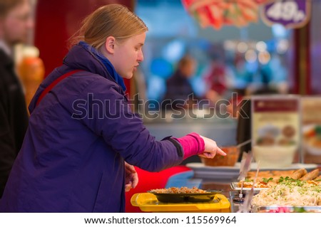 Young woman ordering dishes with vegetables and meat in restaurant