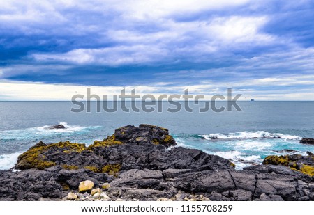 Beautiful rugged volcanic rock Iceland coastline against blue skies with low clouds. Waves pounding shoreline. Blues, greens, aquamarine colors. 