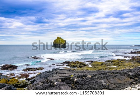 Beautiful rugged volcanic rock Iceland coastline against blue skies with low clouds. Waves pounding shoreline. Blues, greens, aquamarine colors. 