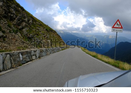 View from a white car of a mountain road without guard rail protection. dramatic cloudy sky.
