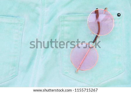 Back pockets blue jeans and rose-colored glasses. Turquoise background
