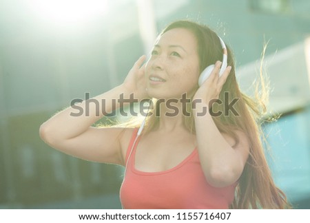 Asian woman smile happily and use phone listen music in the modern city