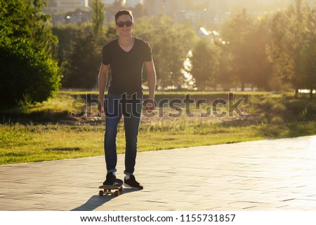 skateboard (longboard) close-up in the hands of a young man in jeans and a black T-shirt in the park