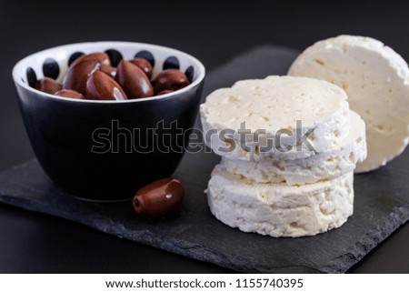 Feta cheese on black slate background with olives - Selective focus on cheese