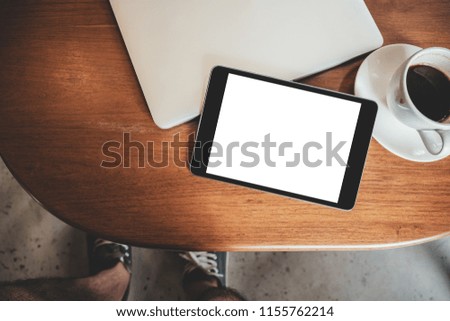 Top view mockup image of a black tablet pc with blank desktop white screen with laptop and coffee cup on wooden table