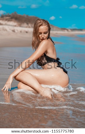 blond girl in swimsuit sitting at sea beach tanning
