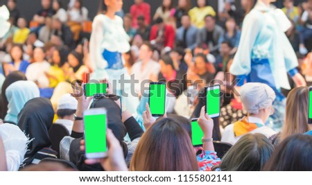 Front row VIP guests people from audience filming record vdo fashion show with mobile smart phone, green screen. Many Guests raise hands up to take photo by many smartphones
