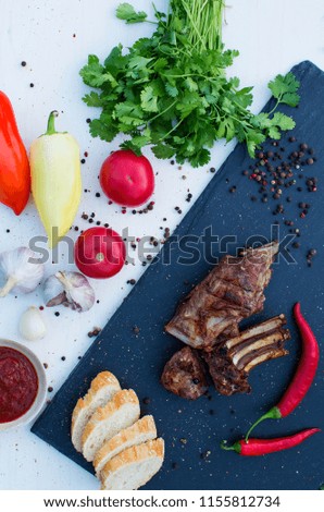 ribs mutton  grilled meat in barbecue sauce and assorted vegetables and many spices on a black slate dish. snack to beer on a dark stone background and white wooden plate. Top view
