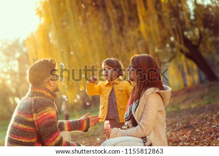Family enjoying an autumn day in nature, parents playing with their child; little girl making soap bubbles