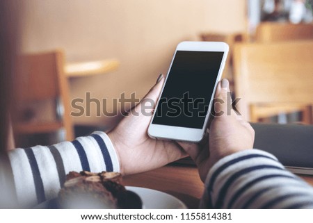 Mockup image of hands holding white mobile phone with blank screen in wooden cafe