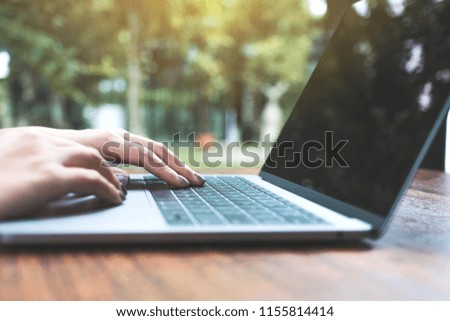 Closeup image of woman's hands working and typing on laptop keyboard on wooden table with green nature background