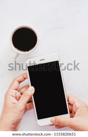 Hand holding smartphone with cup of black coffee on white marble background for media technology and modern lifestyles concept (Vertical image)