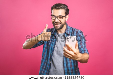 Portrait of a cheerful bearded man taking selfie and showing thumbs up gesture over pink background. Isolated. 