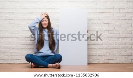 Young Chinese woman over brick wall holding banner stressed with hand on head, shocked with shame and surprise face, angry and frustrated. Fear and upset for mistake.