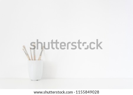 Back to school. Background with stationary. Mug, painting brushes on white wall background, soft home decor. Copy space for text. Empty space for lettering