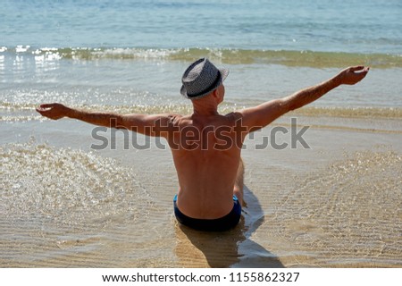 Summer lifestyle portrait of pretty young suntanned man in a hat. Enjoying life and sitting on the beach, time to travel. Looking at the sea