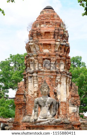 Ancient sitting Buddha image with ruin pagoda at Wat Maha That in Ayutthaya historical park area with trees view and bright sky