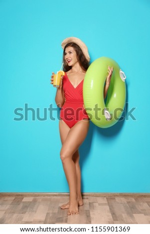 Beautiful young woman with inflatable ring and glass of cocktail near color wall