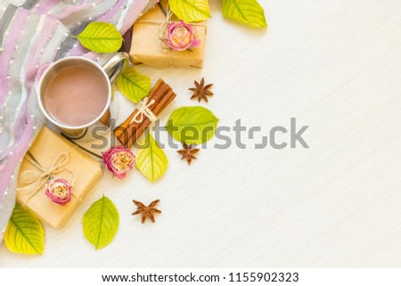 
Autumn composition. Hot chocolate, autumn leaves, badon, cinnamon, cones, roses, gifts, scarf on a light wood background. Flat lay, top view, copy space
