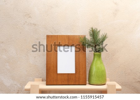 Blank frame and vase with fir branch on table near color wall. Mock up for design