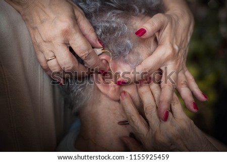 Cropped hand of doctor adjusting woman hearing aid .