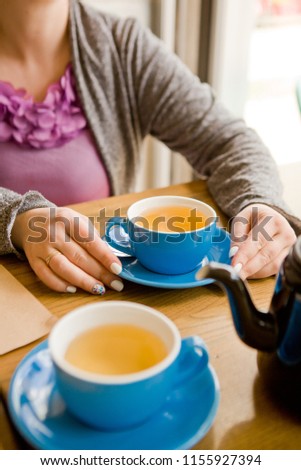 A handsome young woman sits at a wooden table in a loft-style cafe and drinks a cup of coffee or tea. She is inviting and cheerful, enjoying breakfast