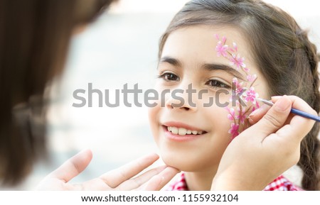 Children face painting. Little girl having fun, making creative floral design outdoors, copy space Royalty-Free Stock Photo #1155932104