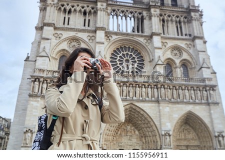 Young stylish woman tourist photographing with old camera standing in front of the famous Notre Dame cathedral in Paris