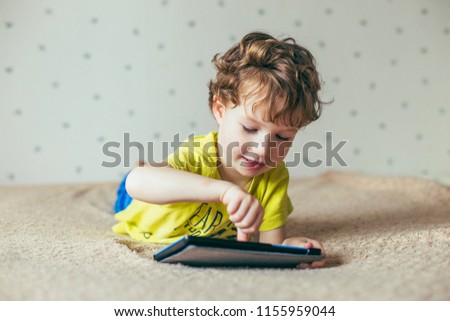 Little cute boy in a green T-shirt playing games on a tablet and watching cartoons. addiction concept