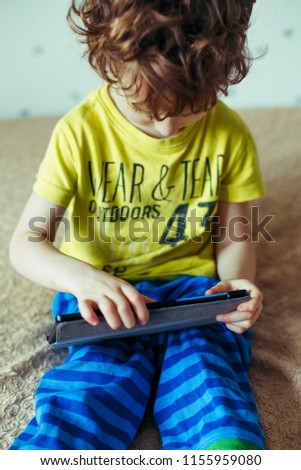 Little cute boy in a green T-shirt playing games on a tablet and watching cartoons. addiction concept
