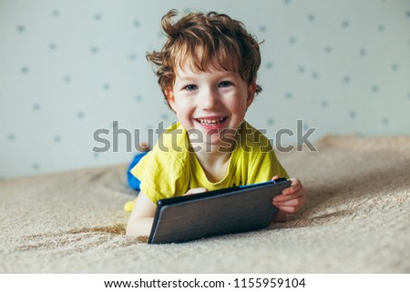 Happy toddler boy having fun playing game on gadget ,Preschool kid sititng on sofa with smiling face watching cartoon on smart phone,Child using cell phone while relaxing at home.