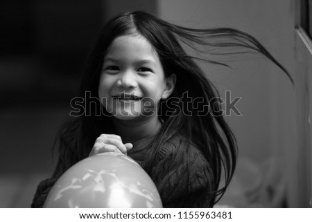 Black and white image of 6 years old Asian girl Blowing balloons.Wind blow her untidy hair.Girl look happy and natural.Concept of Asian  home sweet home.Preteen lifestyle.