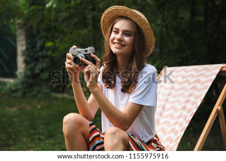 Smiling young girl resting on a hammock at the city park outdoors in summer, taking a picture with photo camera