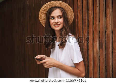 Happy young girl holding mobile phone while standing at the wooden background outdoors