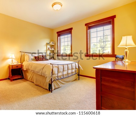 Bright yellow bedroom interior with metal bed frame and two windows.