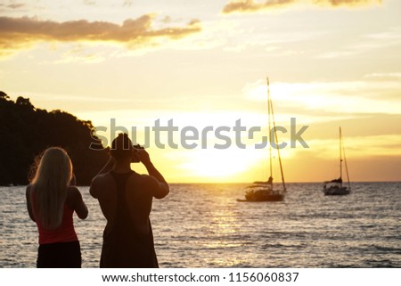 a couple stand watch sunset take photo by the beach