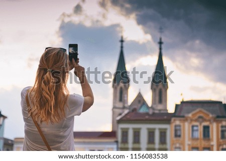 Woman tourist taking a picture of a church on a smartphone. Blond hair woman travelling in European city. 