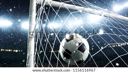 Photo of the ball that flies into a goal on a professional soccer stadium while it's snowing. Stadium and crowd are made in 3D.