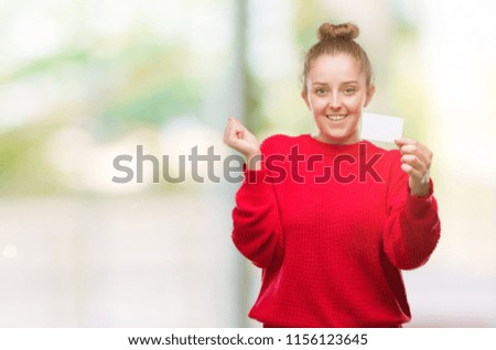 Young blonde woman holding advertising card screaming proud and celebrating victory and success very excited, cheering emotion
